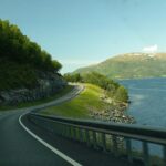 Breathtaking view of a winding road along a Norwegian fjord, surrounded by water and lush greenery.
